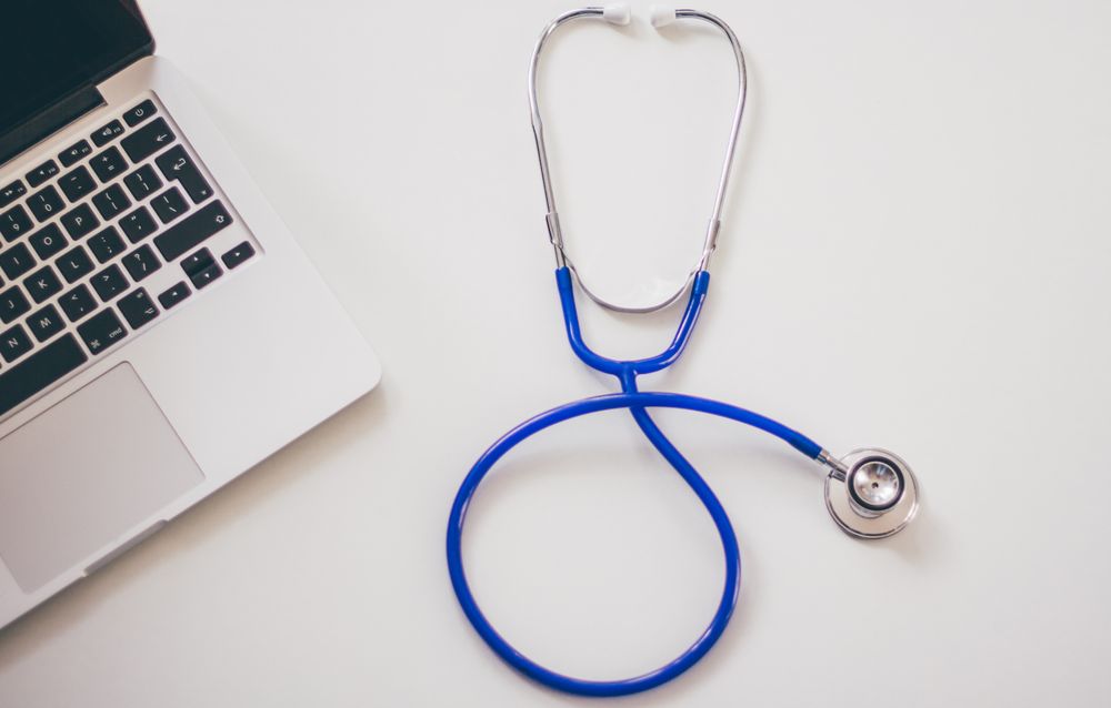 A blue stethoscope beside an open laptop