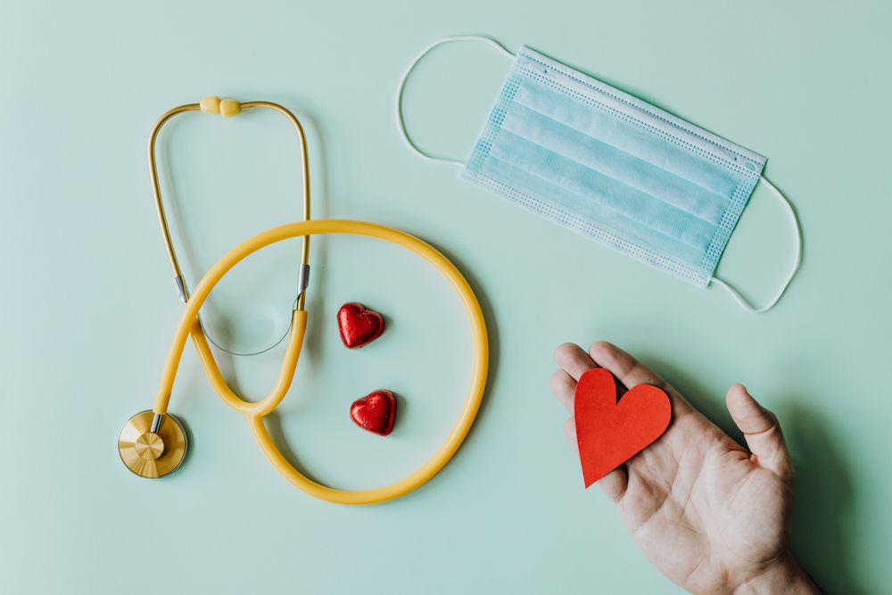 A blue face mask beside a stethoscope and a paper heart